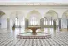 Alternativ-Text DE: Foto: Ansicht der Ausstellung "Palast. Ayzit Bostan" im historischen Raum der Rathausgalerie. Im Zentrum steht ein historischer Brunnen aus rotem Marmor mit Löwenköpfen. Schwarz-weißer Kachelboden mit geometrischen Mustern umgibt ihn.